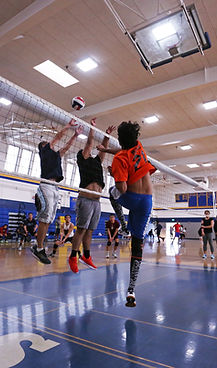 Players jumping at the net in a youth and adult volleyball class.