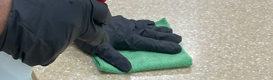 Hand in black glove wiping countertop with green cloth