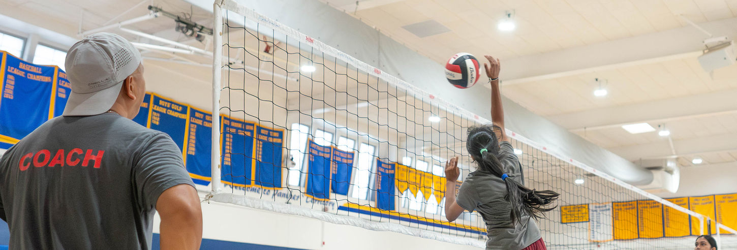 Coach watches a volleyball player spiking ball in a gym.