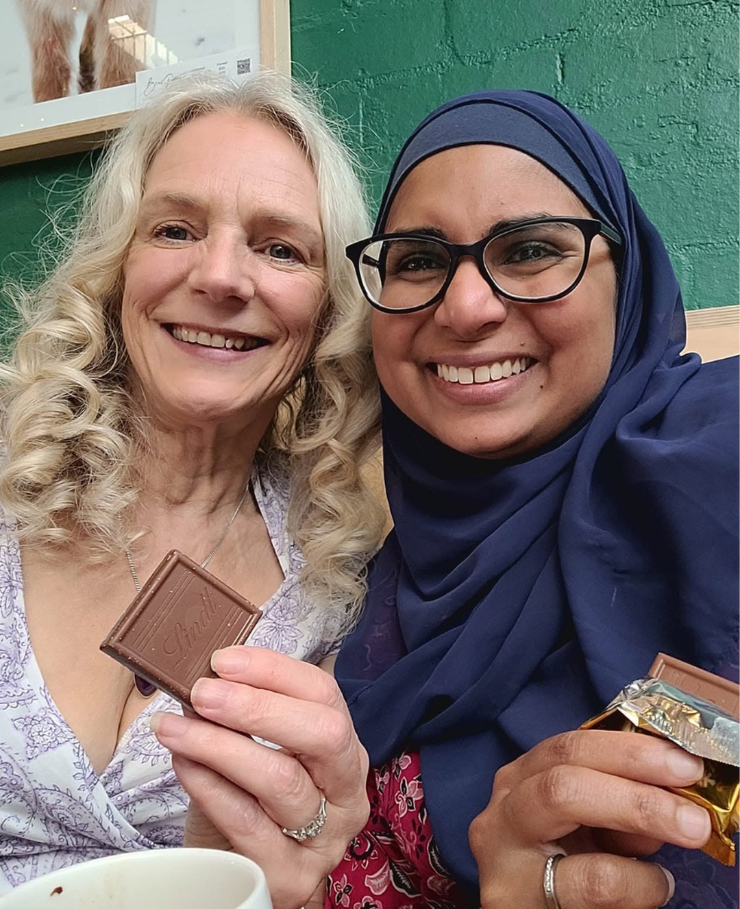 Two women smile and hold up squares of chocolate during a Chocolate and Coffee Day encounter.