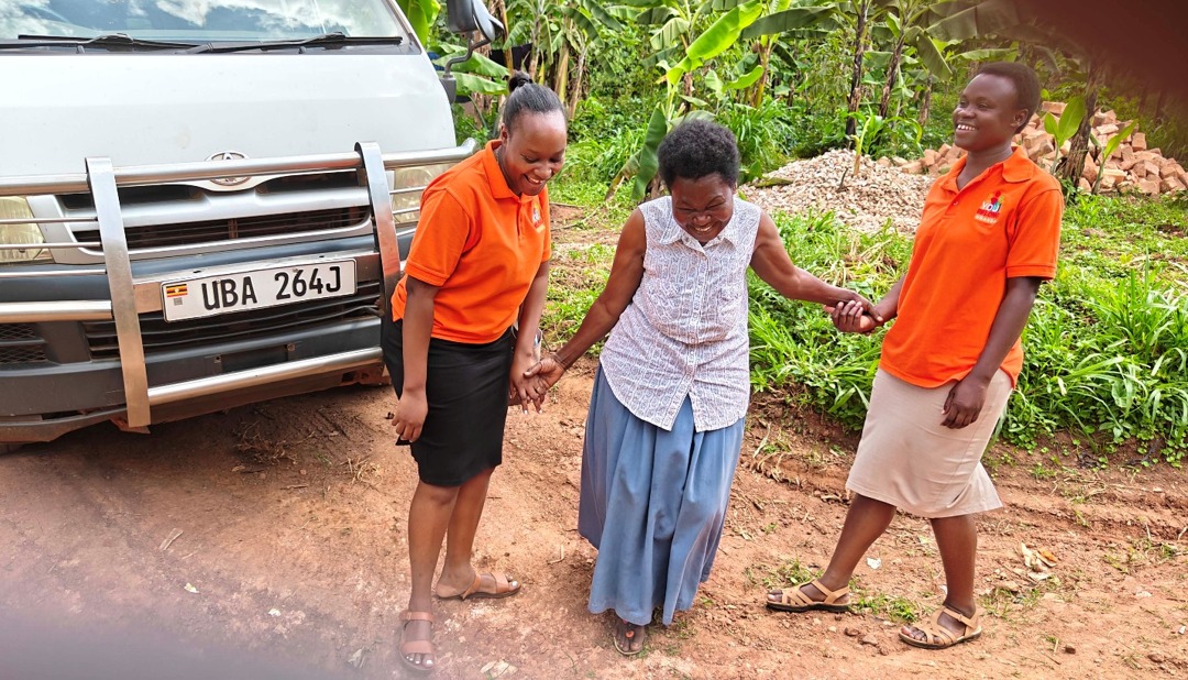A caregiver holds hands with a YouBelong social worker and mental health nurse in orange shirts beside the YouBelong bus.