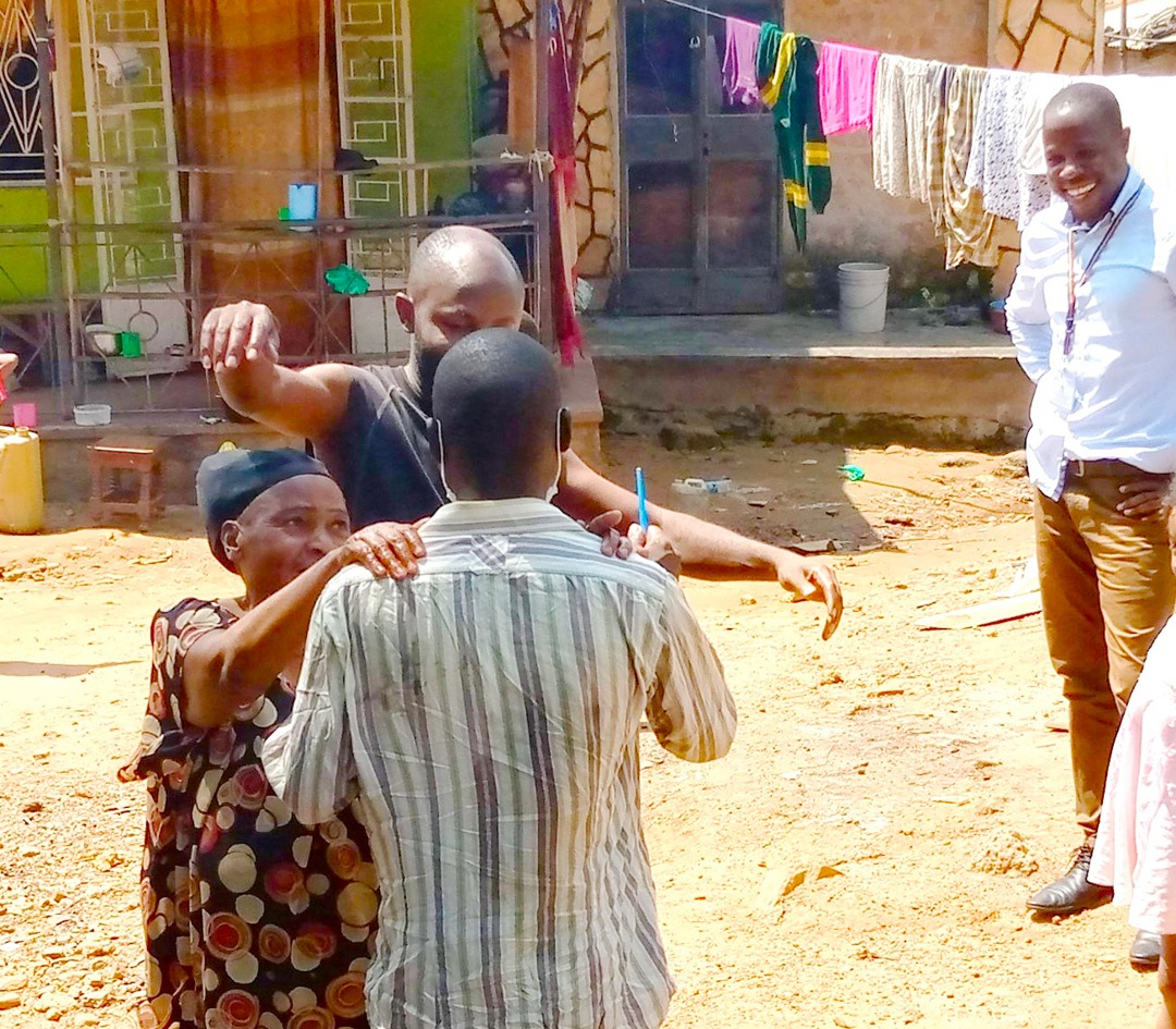 A mother embraces her son as he returns home from hospital in Kampala, while a YouBelong social worker smiles nearby.