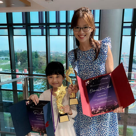 Piano student receiving a competition award with teacher at Melodious Piano Studio Singapore