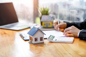 Someone working at desk with replicas of houses, filling out paperwork on clipboard