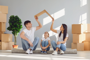 Happy family of three sitting on floor surrounded by moving boxes