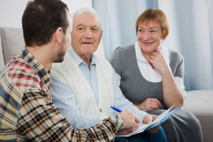 Older couple talking with younger gentleman on couch over paperwork