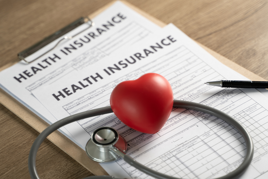 Health insurance forms on desk with red foam heart and stethoscope