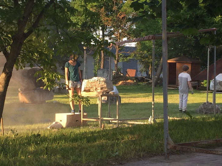 Девојка која стоји на кутији са гас маском и гледа у камен у великом дворишту окруженом зеленилом.