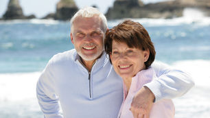Pareja de adultos mayores sonrientes y abrazados en una playa soleada, representando la sexalescencia y la madurez activa.