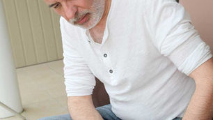 Older man touching his knee with a pained expression, a possible symptom of arthritis or osteoarthritis.