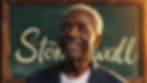 A black older LGBTQ+ person stands in front of a chalk board with the word 'Stonewall' written behind him.