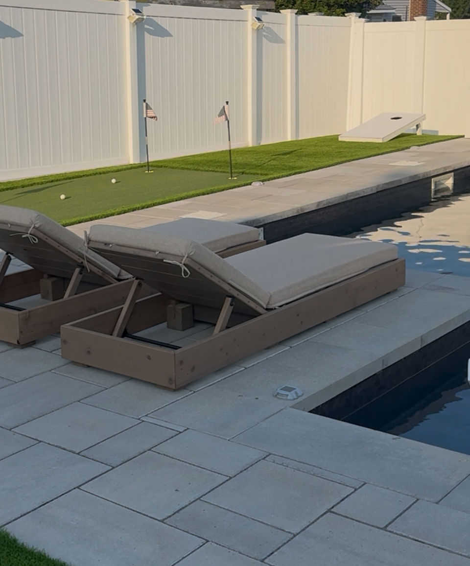 Loungers next to a putting green and pool in a backyard.
