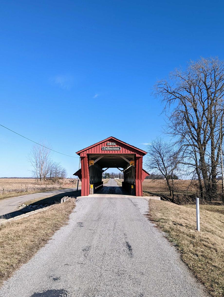 Red covered bridge over a road under a clear blue sky.