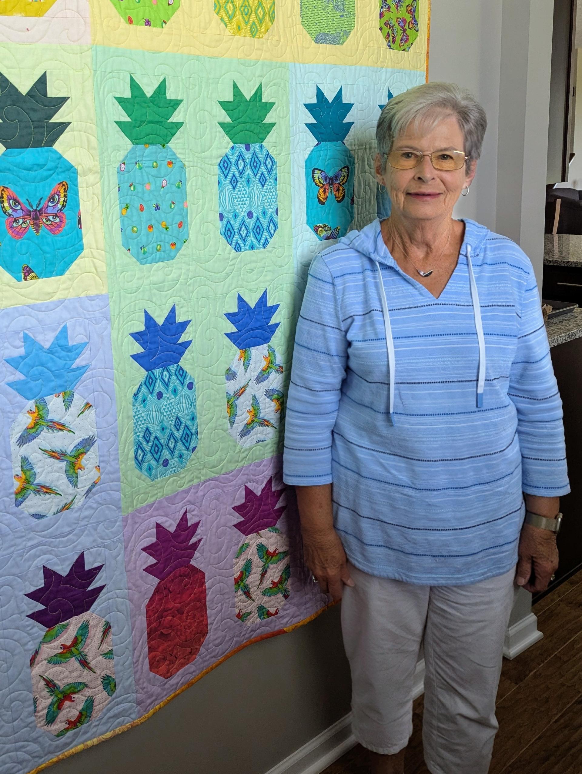Woman standing next to a colorful pineapple quilt quilt.