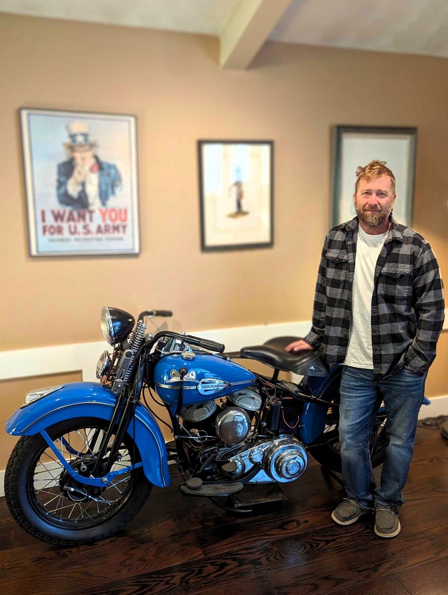 Man standing next to a blue vintage motorcycle