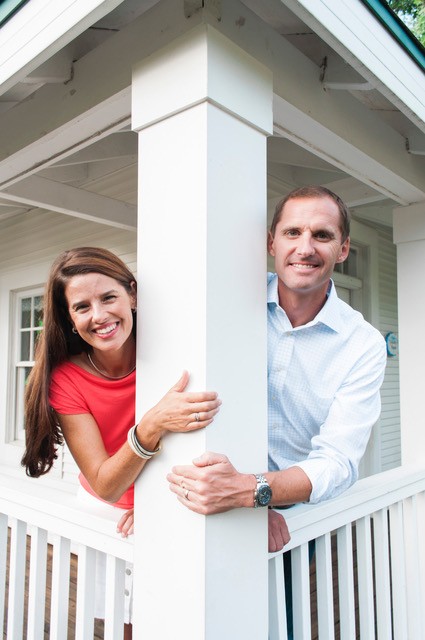 Smiling couple peeking around a white porch pillar.
