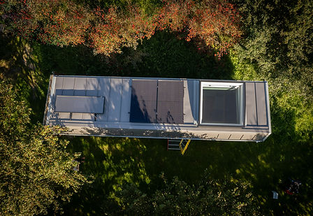 Drohnenaufnahme von Waldkindergarten zwischen Bäumen mit Solarpanelen und grossem Oberlicht.