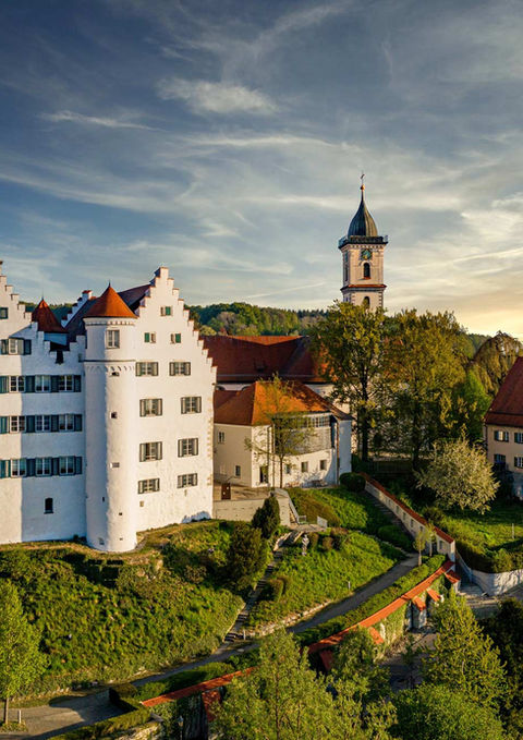 Weißes Schloss auf Hügel, Kirche und Stadt bei Sonnenuntergang, Tourismus.
