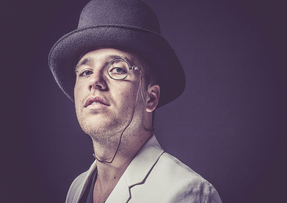 Mann mit Hut, Monokel und hellem Jackett blickt ernst