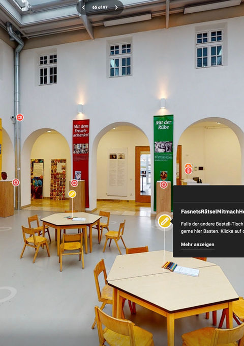 Geräumiger Ausstellungsraum für Kinder mit kleinen Tischen und bunten Bannern.