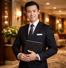 A hotel manager wearing a suit and holding a folder while standing in a hotel lobby. Begin