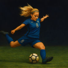 A blond woman in a blue soccer uniform kicking a soccer ball