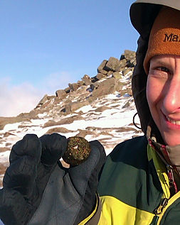 Smiling hiker holds energy ball on top of a snowy Scottish mountain.