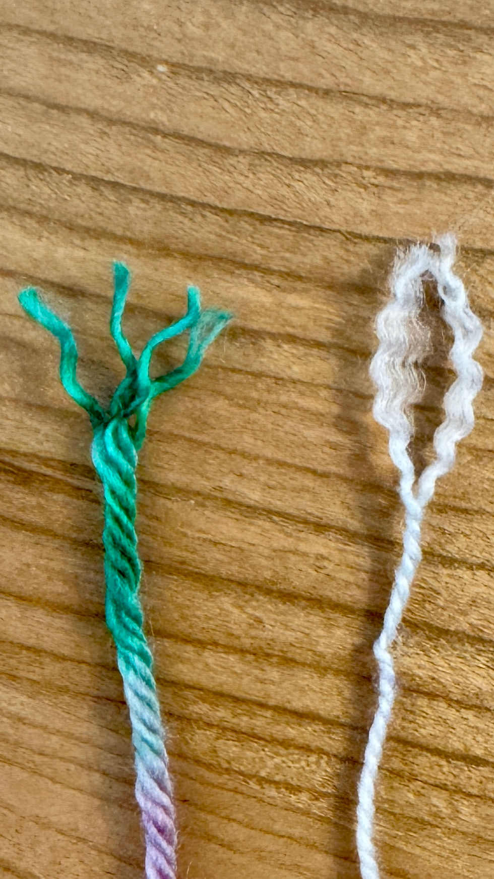 Green and white yarn untwisted on wood surface. The green yarn shows colorful strands, while the white yarn loops, displaying texture.