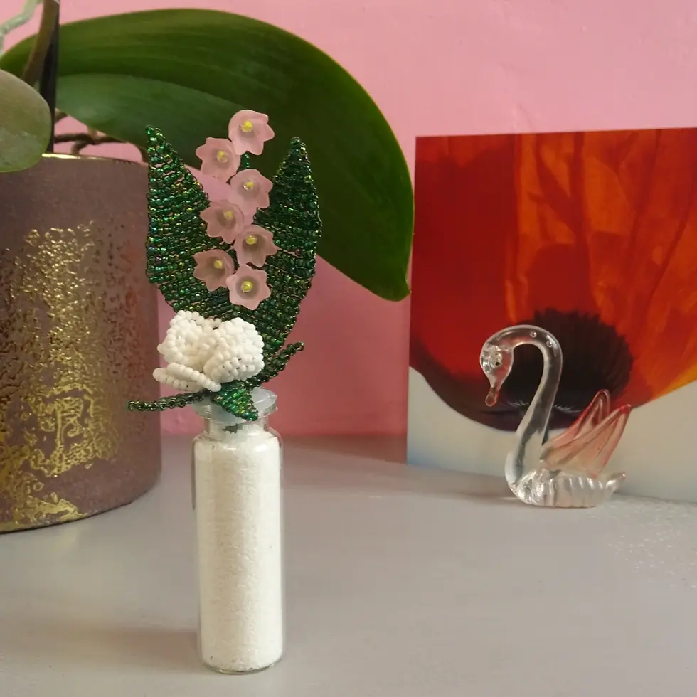 Miniature : Brin de muguet rose et rose blanche en perles dans un flacon en verre posé sur une étagère
