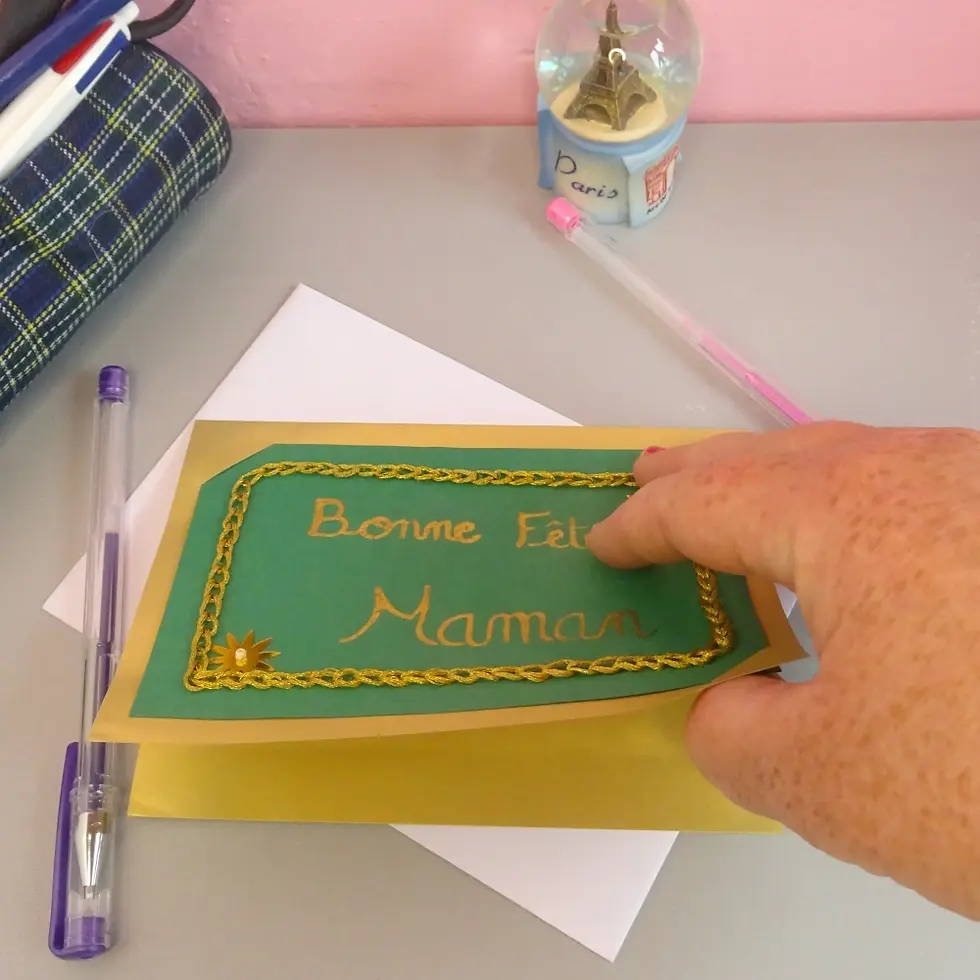 Miniature : Carte bonne fête maman verte et doré ouverte à la main, sur un bureau prête à recevoir un mot doux