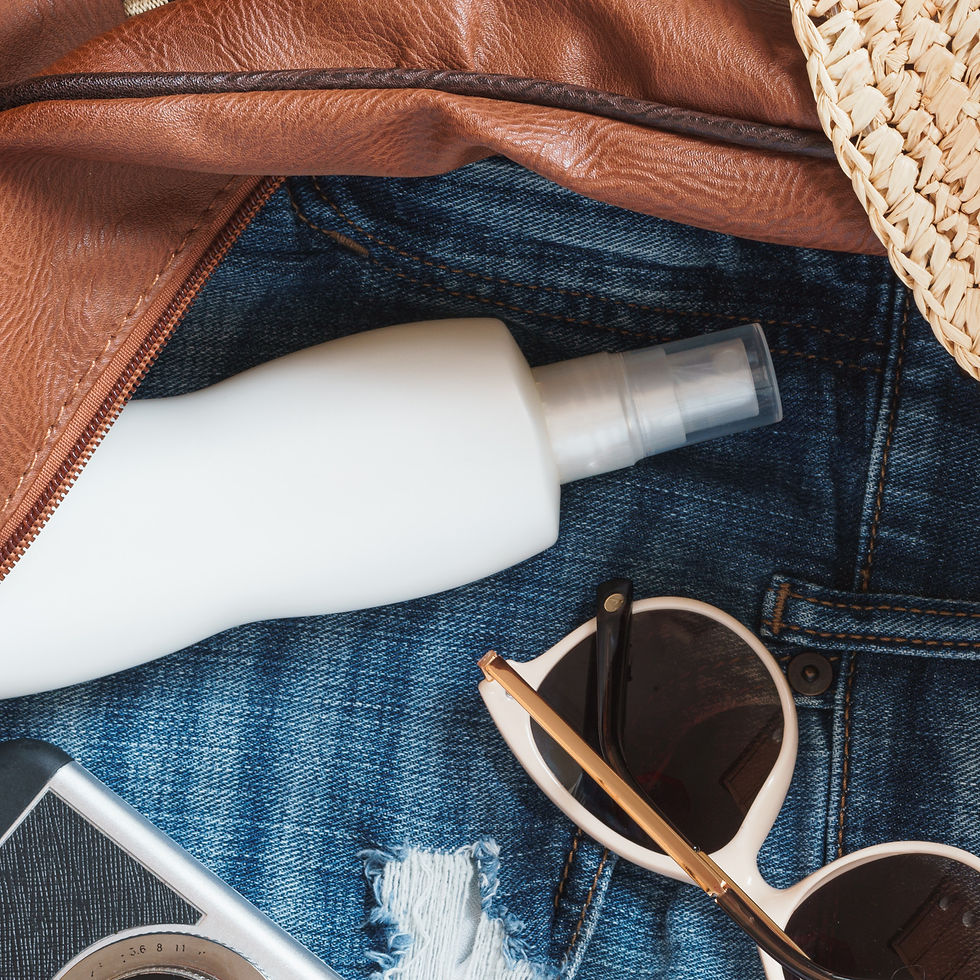 Accessoires d’été dans un sac en jean : crème solaire, lunettes de soleil, appareil photo, cuir brun et paille.