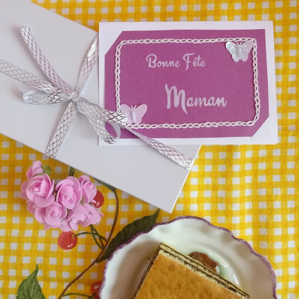 Miniature : Carte bonne fête maman violette et blanche glissée sous le ruban d’un cadeau, avec bouquet de fleurs et part de gâteau