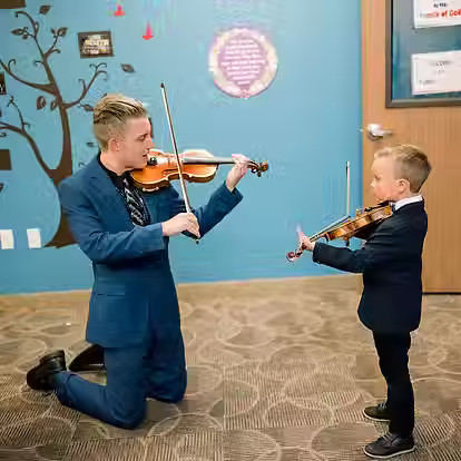 teacher on knees playing violin with young student
