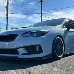 Low-angle view of a lowered white sedan with multi-spoke wheels and color-shifting LED headlights parked outside Precision Wraps; tinted windows and shop signage in background.