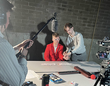 Behind-the-scenes photo of the director helping the actor in front on a desk in between scenes.