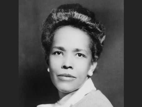 Black and white portrait of a woman with an elegant hairstyle against a dark background. She appears calm and composed, wearing a light top.