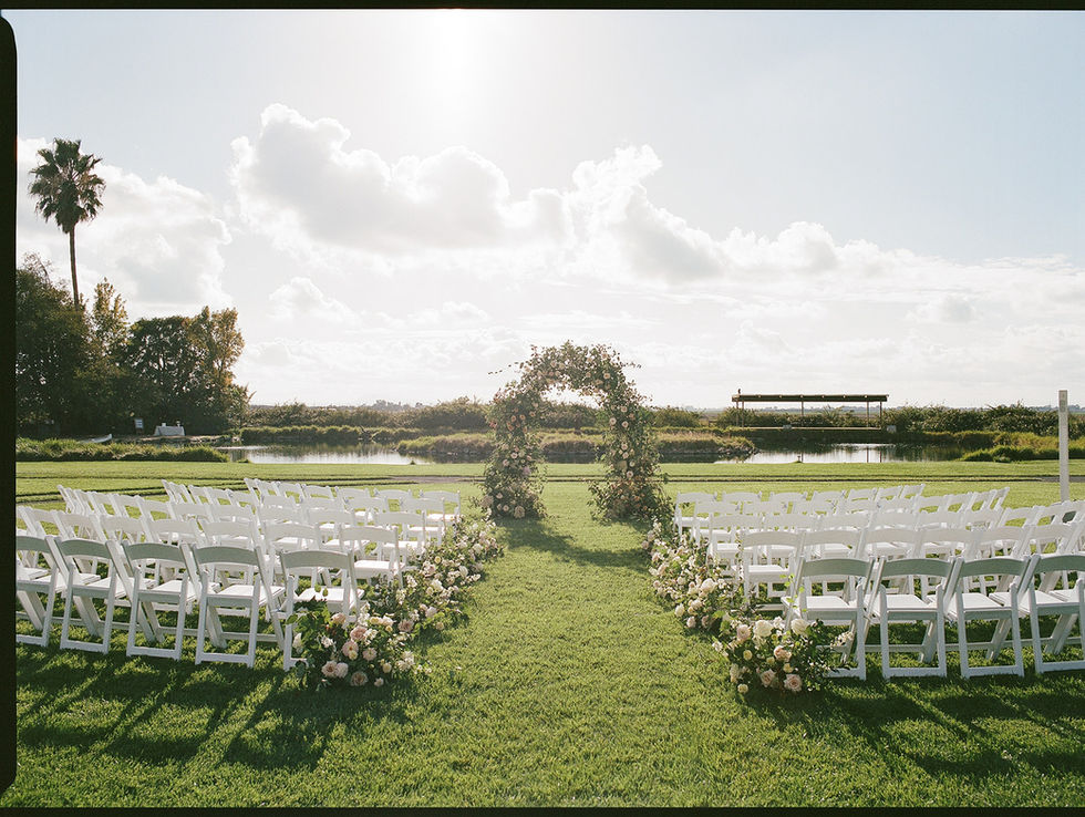 rows of white chairs are lined up in front of a floral arch