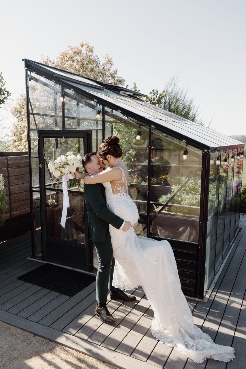 a bride and groom are kissing in front of a greenhouse