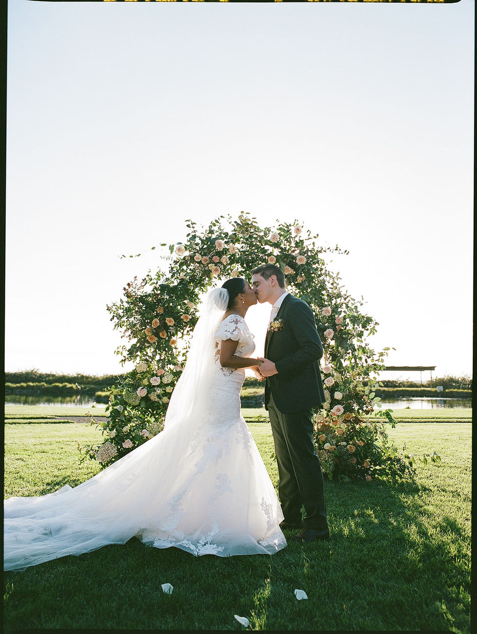 a bride and groom kiss in front of a floral arch