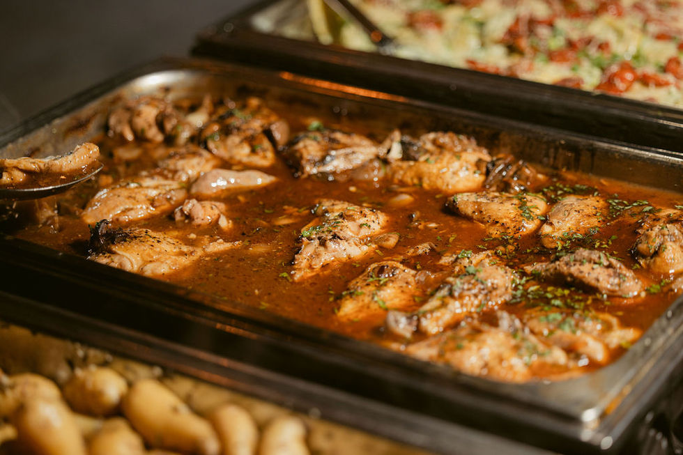 a tray of chicken in a sauce with potatoes in the background