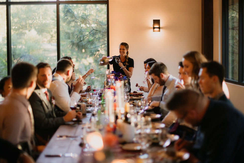 a woman is pouring wine into a glass at a long table
