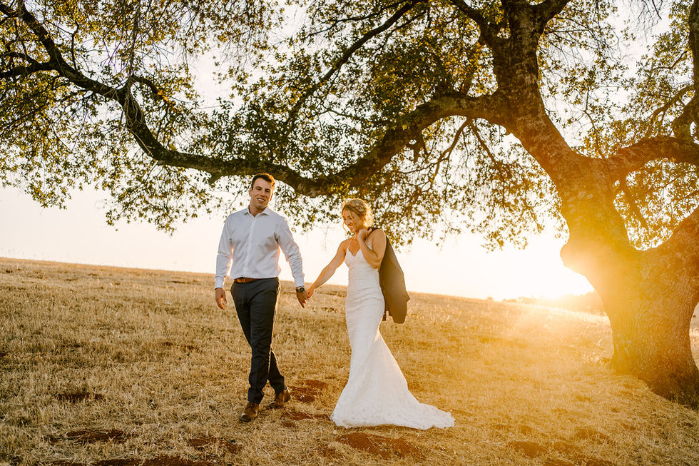 a bride and groom holding hands in a field at sunset