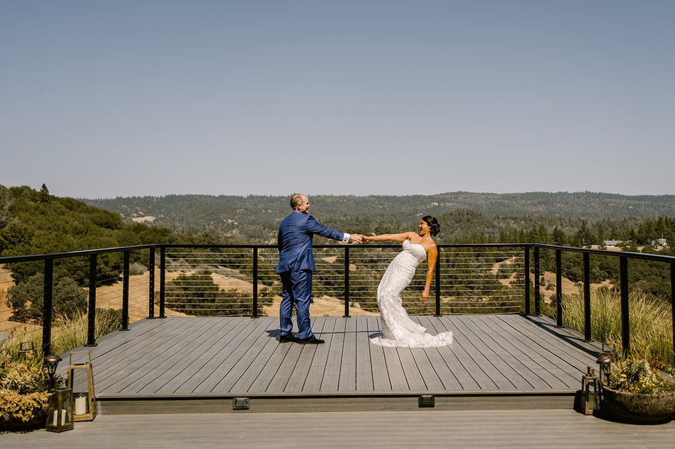 a bride and groom hold hands on a balcony overlooking a forest