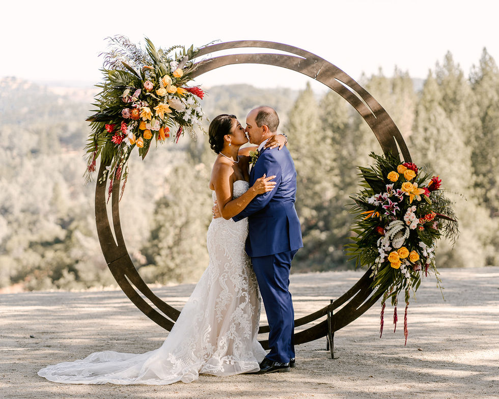 a bride and groom kiss under a floral arch