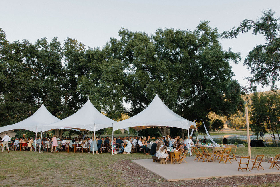 a group of people are sitting at tables under white tents
