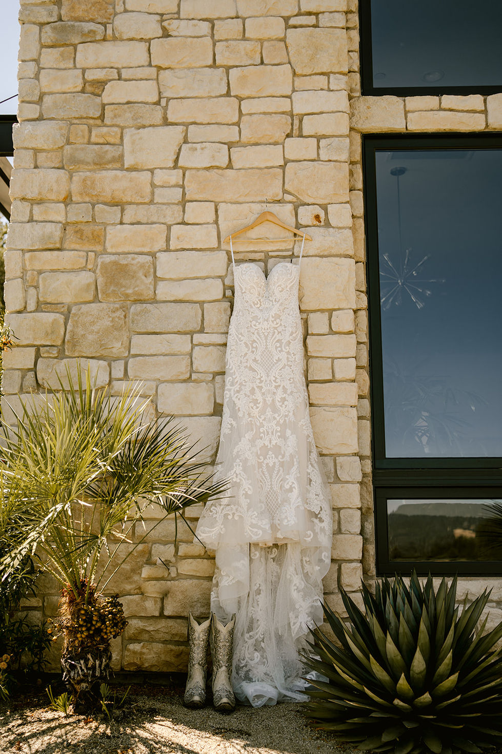 a wedding dress hangs on a wooden hanger in front of a stone wall