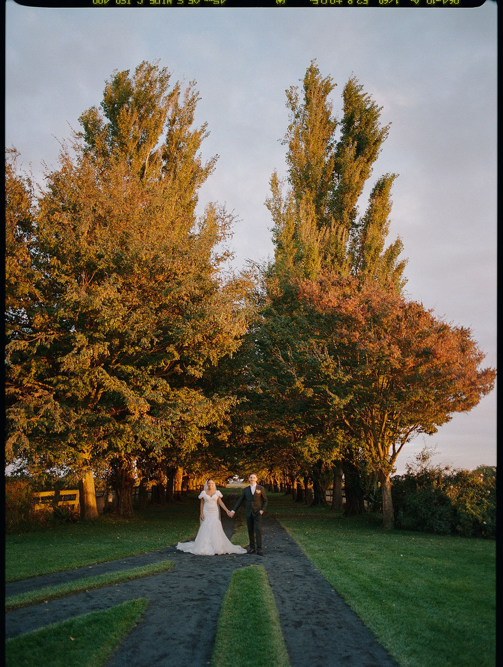 a bride and groom are walking down a path surrounded by trees