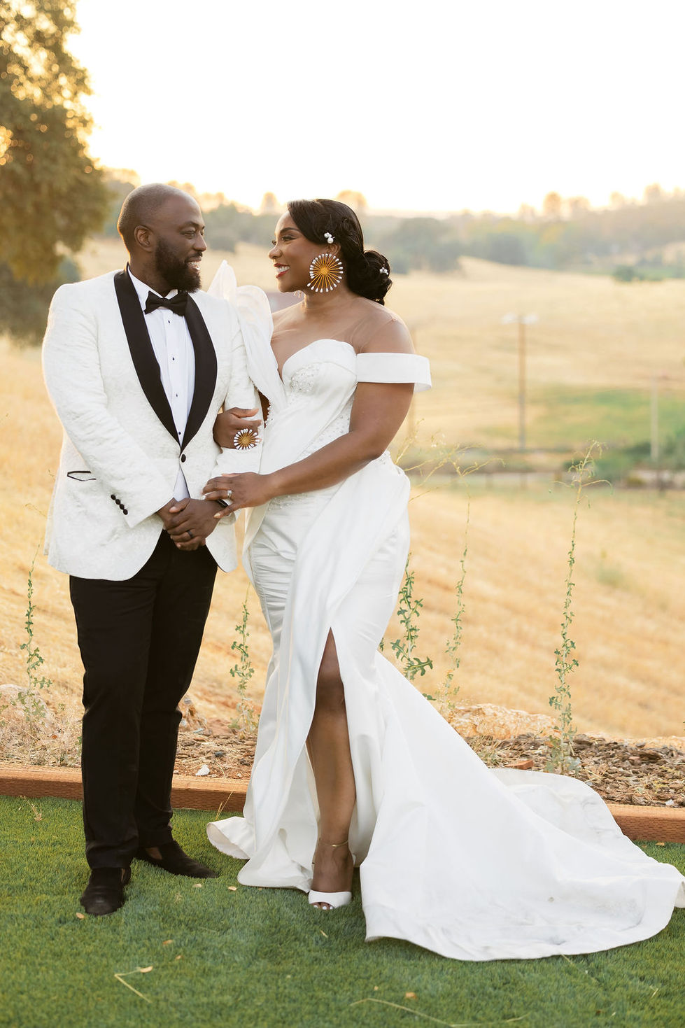 a bride and groom standing next to each other in front of a field