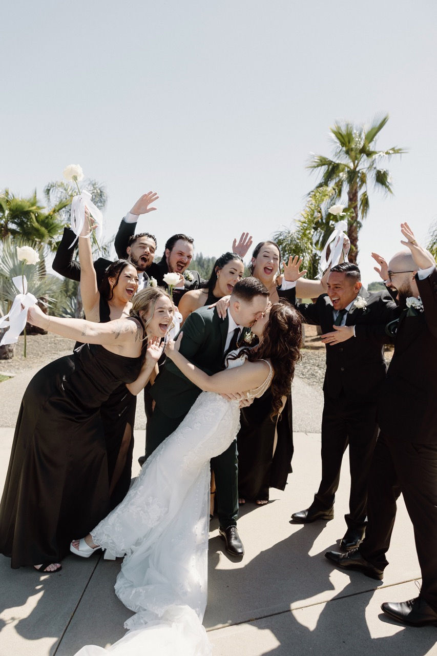 a bride and groom are kissing surrounded by their wedding party