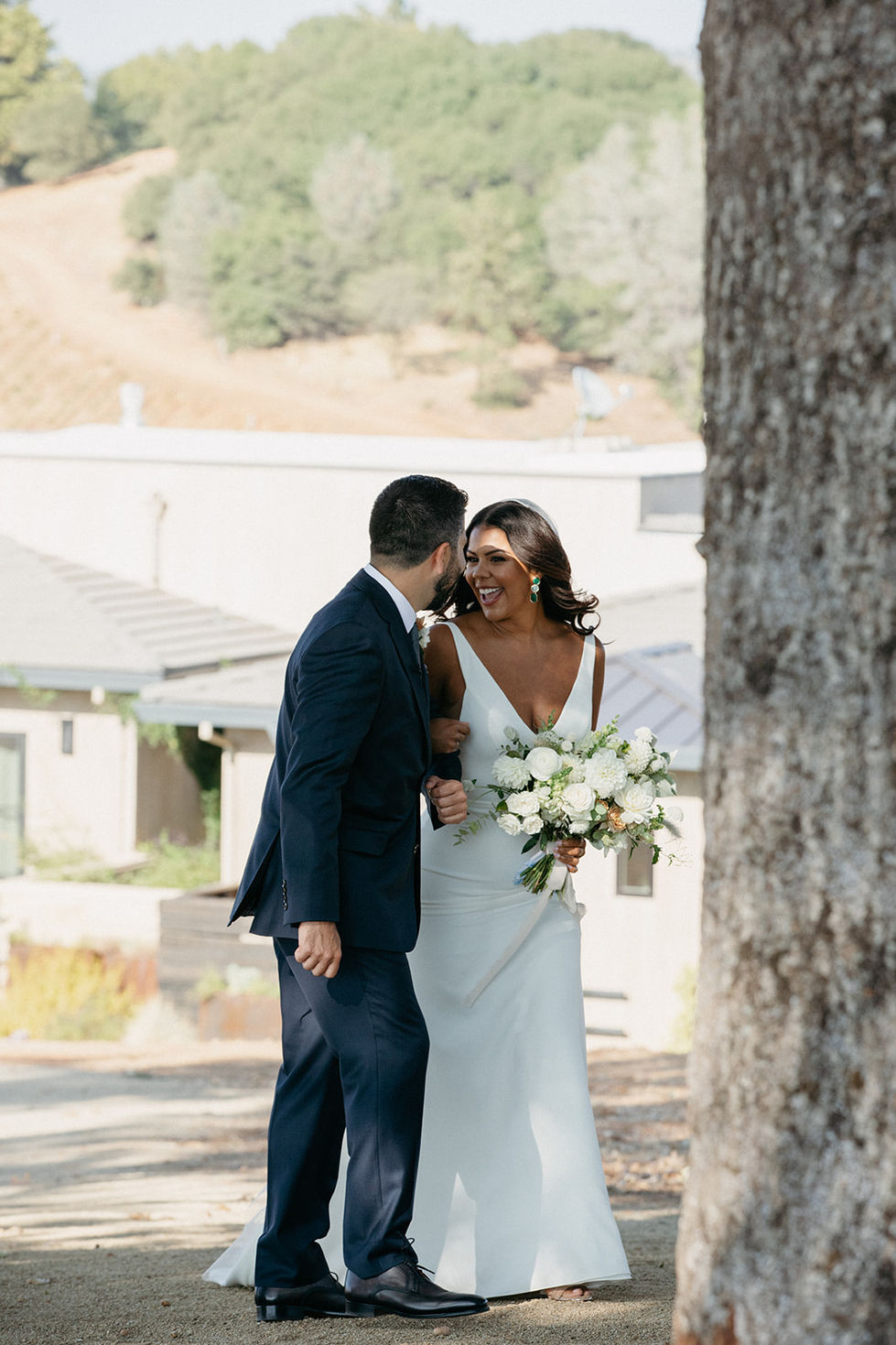 a bride and groom are laughing in front of a tree